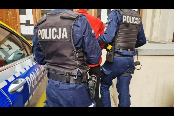 zdjęcie-policjanci prowadzą zatrzymanego, dzień, obok radiowóz policji